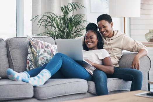 Nothing says romance like a cosy weekend at home. Shot of a young couple using a laptop while relaxing on the sofa at home.