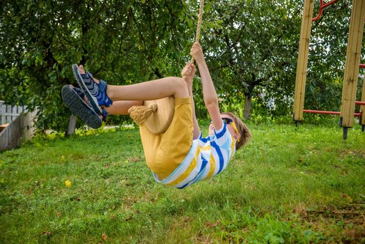 Happy little boy is having fun on a rope swing which he has found while having rest outside city. Active leisure time with children