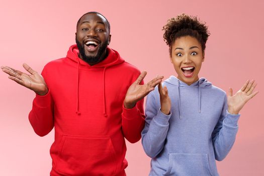 Guys receive nice surprise. Two attractive carefree surprised happy african man woman clapping hands joyfully greeting welcoming guests inviting people joing party standing friendly pink background