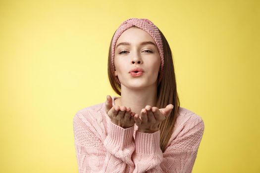 Happy valentines day. Charming romantic and sensual young flirty woman in knitted headband, sweater extending palms near folded lips sending air mwah, blowing kiss tender and gentle