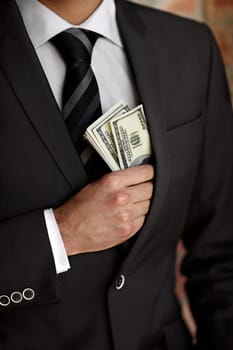 Hes not above accepting a bribe. Cropped shot of a man tucking a wad of cash into his jacket.