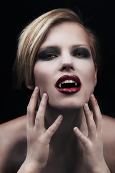Creature of the night. A seductive female vampire with blood red lips against a dark background.