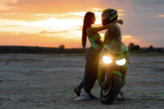 Couple embracing near motorbike on beach at sunset