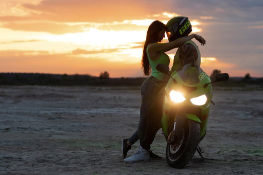 Couple embracing near motorbike on beach at sunset