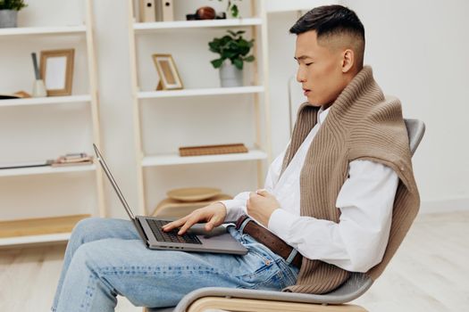 Asian man sitting in a chair in a room with a laptop on his lap technologies