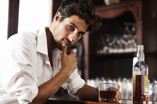 Gathering thoughts after a hectic day. Young sophisticated man drinking whiskey alone at the bar.