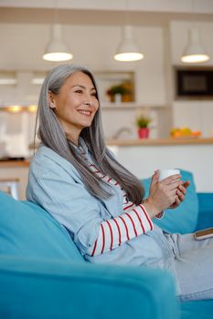 Cheerful woman with cup of coffee sitting on couch at home