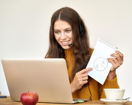 Happy woman in headset speaking by conference call and video chat on laptop in office