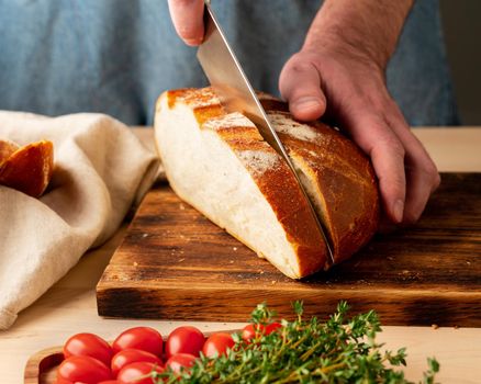 Faceless man cutting fresh home-baked crusty bread with large knife
