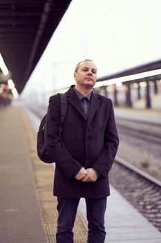 Train Station. Mature man in business clothes and coat is standing on platform