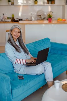 Cheerful woman sitting on couch and using laptop at home