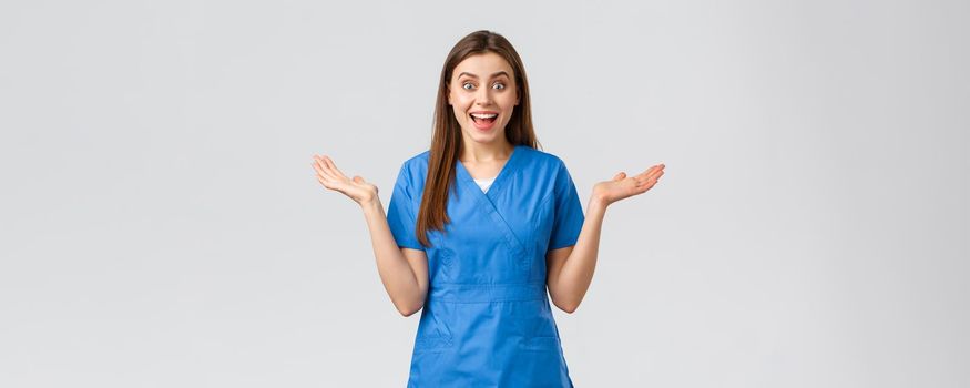 Healthcare workers, prevent virus, insurance and medicine concept. Surprised happy female nurse or doctor hear wonderful news, clap hands open mouth and look fascinated, grey background