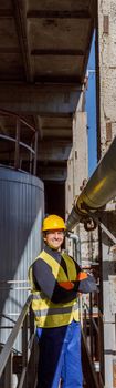 Joyful male engineer standing near metal pipe at factory