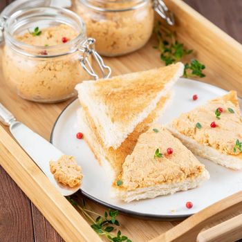 Fresh homemade chicken pate on toasted bread on tray over rustic background, side view