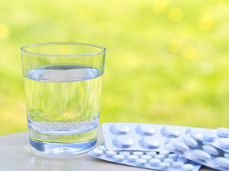 Glass of water and of pills on table on green nature background. Allergic to flowers and pollen. Empty space, defocused.