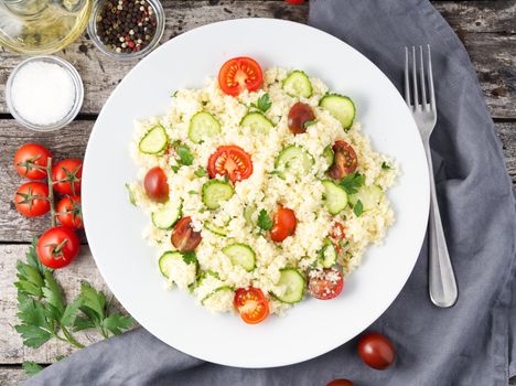 fresh diet vegetable salad with couscous, tomatoes, cucumbers, parsley, dark rustic wooden table, top view