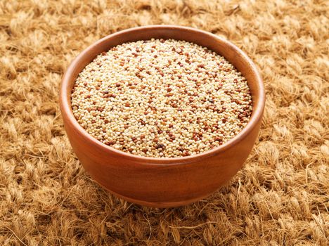 Raw Quinoa in wooden bowl, superfood. Brown sisal mat background, side view.
