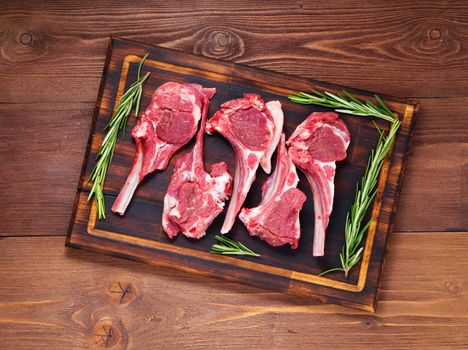 Raw lamb cutlets on bone on dark brown wooden background, lamb ribs, top view.