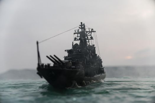 War concept. Night battle scene at sea. Dramatic toned clouds effect. Silhouette of the battle ship at sunset. Miniature creative table decoration. Selective focus