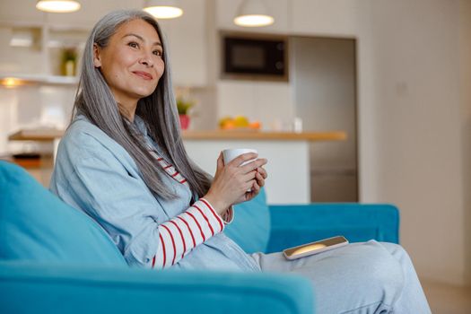 Smiling woman with cup of coffee sitting on couch at home