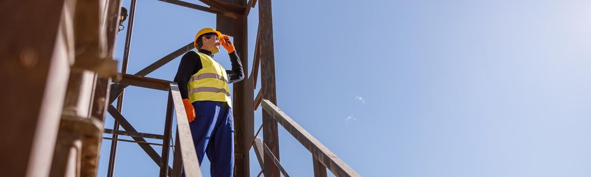 Male worker standing on top of stairs under blue sky