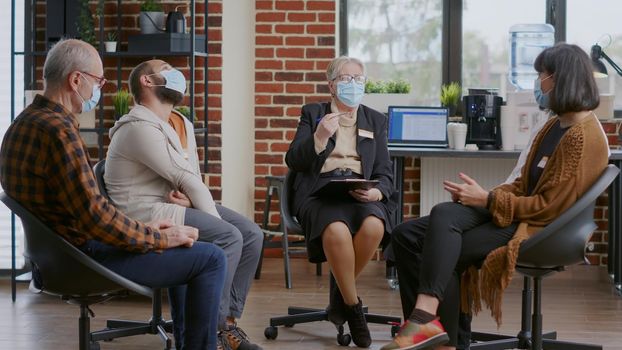 Woman therapist giving advice to people at aa group meeting, wearing face mask