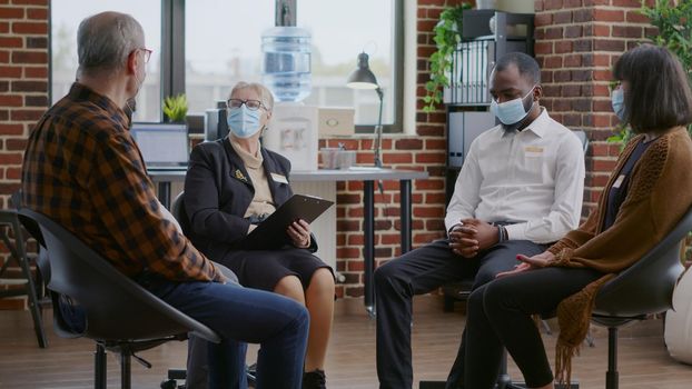 Therapist giving advice to multi ethnic group of people with face mask at aa meeting