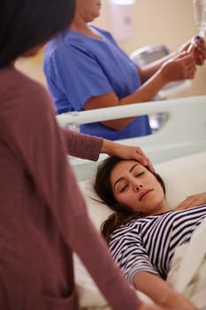 Shot of a woman touching her friends forehead as she lays in her hospital bed.