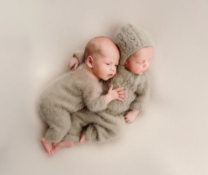 Twins newborn babies sleeping wearing knitted costumes and hugging each other studio portrait. Siblings brothers infant children napping together