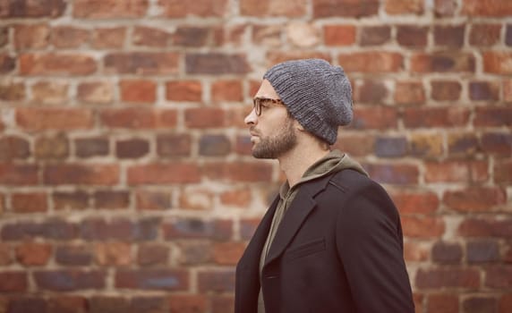 Urban style. Shot of a handsome young man in trendy winter attire standing in front of a brick wall.