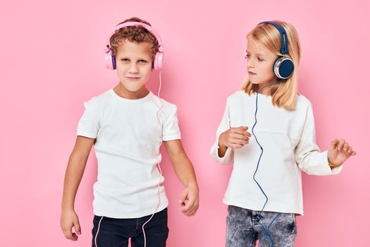 Stylish little boy and cute girl stand next to in headphones pink color background