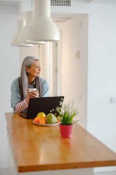 Smiling woman drinking coffee and using laptop at home