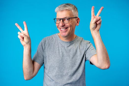Senior man showing victory sign over blue background