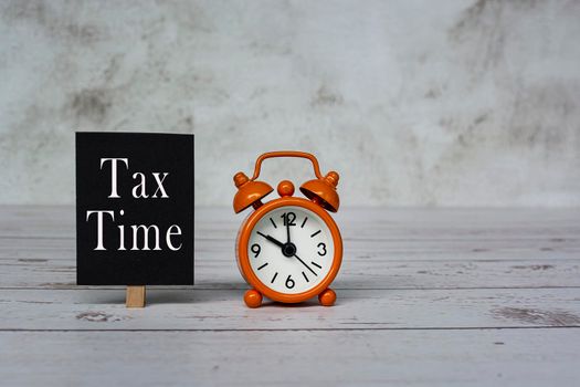 Tax time text on black notepad and alarm clock set at 10 o'clock on wooden desk.