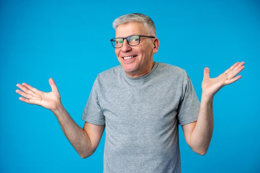 Middle age man over blue background clueless and confused expression with arms raised