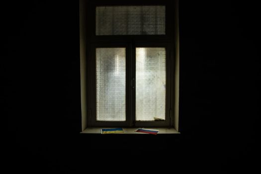 Conceptual photo of war between Russia and Ukraine. Ukraine and Russia flags on windowsill at night. Old creepy room with window. Explosion outside.