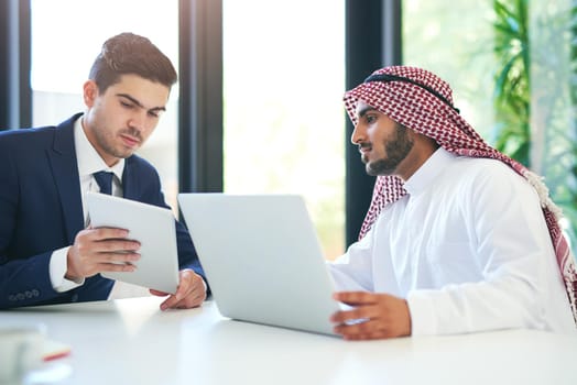 Complimentary skill sets for a successful collaboration. Shot of a young muslim businessman using a laptop and digital tablet with his colleague at work.