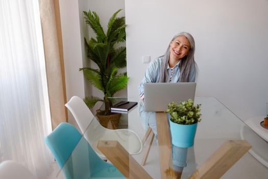 Cheerful woman sitting at the table with laptop at home