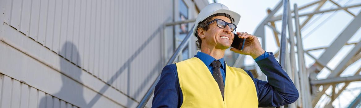 Cheerful male engineer talking on cellphone outdoors at factory