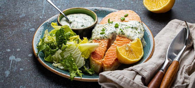 Healthy food meal cooked grilled salmon steak with white dill sauce and green salad leafs