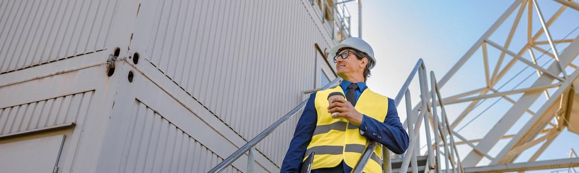 Male engineer with coffee cup standing on stairs outdoors