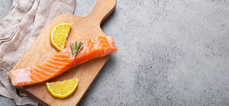 Raw salmon fish fillet with lemon wedges and rosemary on wooden cutting board