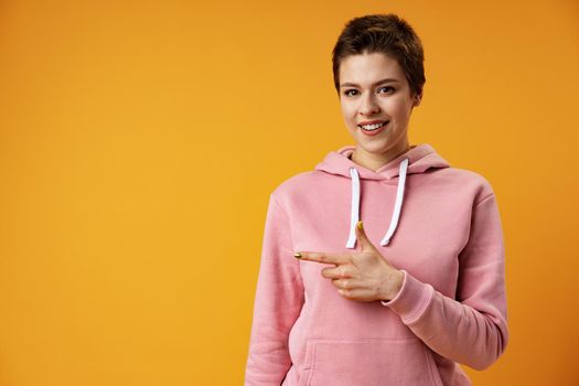 Young woman with short hair over studio color background pointing finger to the side