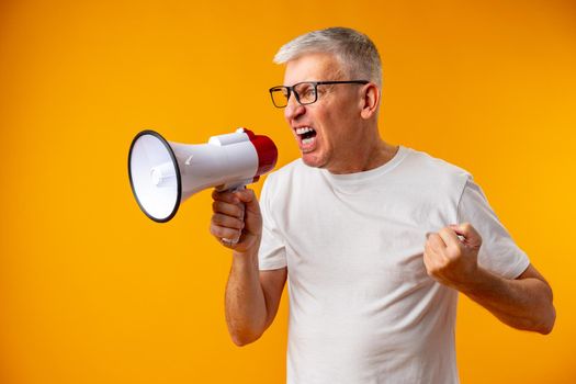 Portrait of mature man shouting with megaphone against yellow background