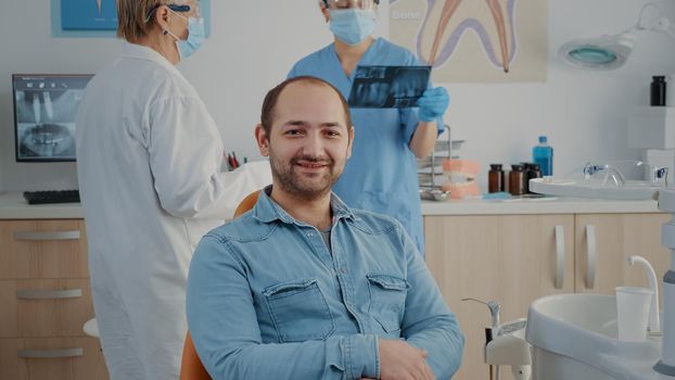 Portrait of patient sitting in dental chair at oral care clinic, looking at camera and smiling. Caucasian man having stomatological appointment with dentistry specialist in cabinet.