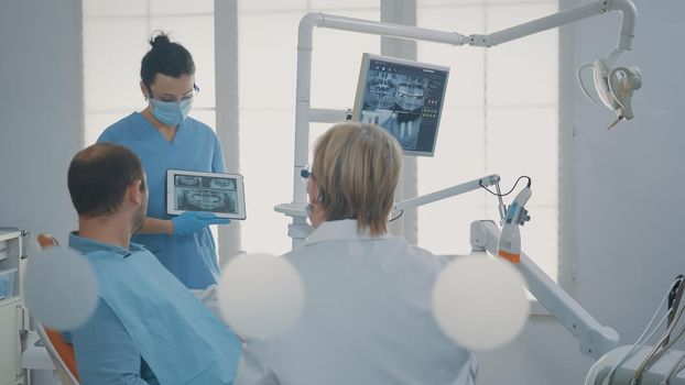 Dentist pointing at denture radiography on digital tablet