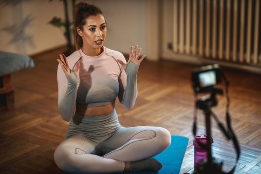 Young beautiful sporty woman vlogger is making video training for blog about healthy living and exercises in front of a camera at home. 