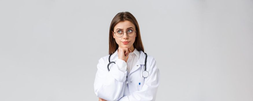 Healthcare workers, medicine, insurance and covid-19 pandemic concept. Concerned unsure young female doctor making serious decision, smirk look up thoughtful, smirk displeased, thinking tough choice