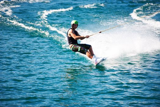 A young man wearing a helmut and lifejacket wakeboarding on a lake. A young man wearing a helmet and lifejacket wakeboarding on a lake.
