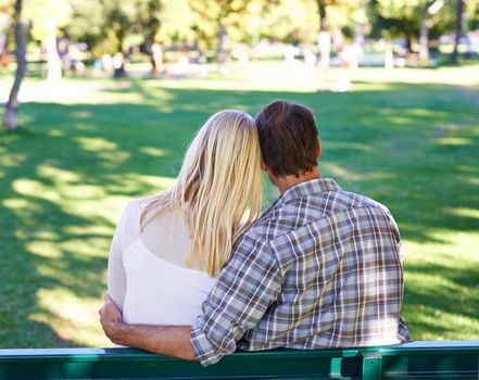Keeping young love alive. Rearview of an affectionate young couple sitting on a park bench.